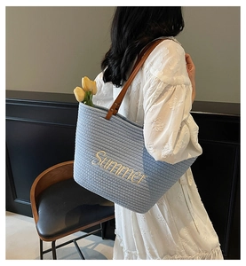 Detail of light blue straw tote with yellow Summer embroidery and brown leather handles