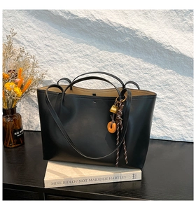 Detailed view of black matte leather tote bag with elegant gold lock and orange charms