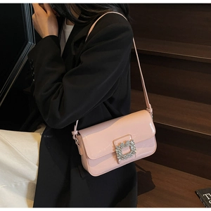 Close-up of a pink patent leather handbag with a luxury crystal buckle worn by a model
