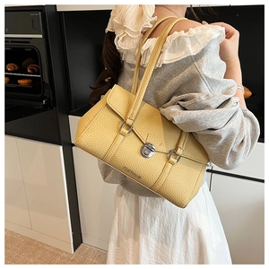 Detail of yellow pebbled leather shoulder bag with silver twist lock on a minimalist setup
