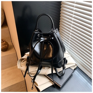Detail of glossy black leather bucket bag showing drawstring closure and ribbon bow