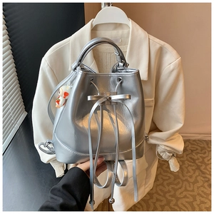 Silver bucket bag with bow drawstring and cute charm detail on a white blazer background