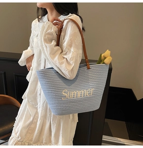 Detail of blue straw tote bag featuring yellow Summer embroidery and brown leather strap