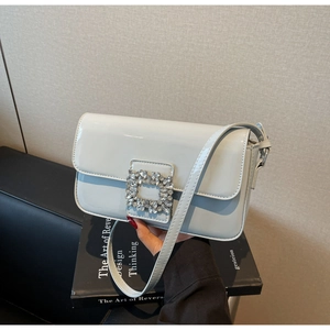 Close-up of sparkling rhinestone square buckle on light blue patent leather bag