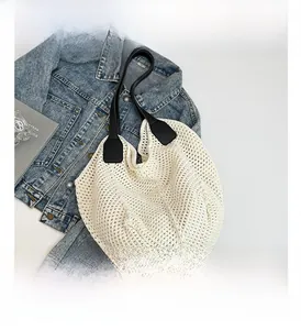 Close-up of white knitted tote bag with black leather straps on denim background