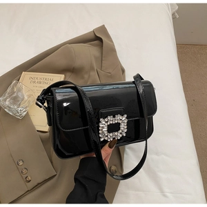 Close-up of black patent leather shoulder bag with a large sparkling rhinestone buckle