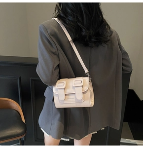 Detail of a beige PU leather crossbody bag with dual straps and brand logo on a model
