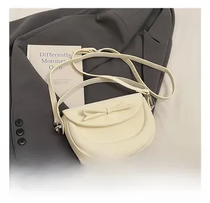 Gros plan du sac besace blanc crème montrant le nœud en cuir et les crochets