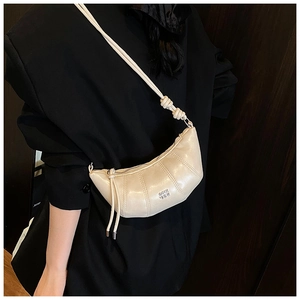 Close-up of quilted cream dumpling bag on black blazer showing shiny PU leather texture