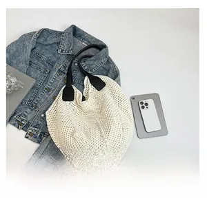 Top-down view of a beige woven knit tote bag with black leather handles and daily essentials