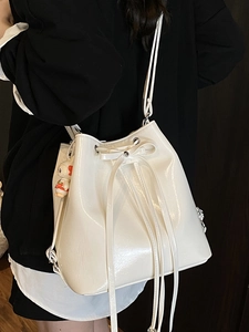 Glossy white bucket bag with drawstring closure and bow detail worn by a model