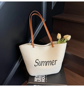 Detail of a beige woven tote bag with brown leather handles and Summer embroidery