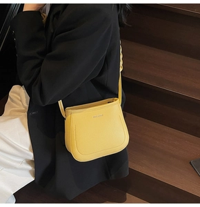 Yellow saddle-shaped crossbody bucket bag in lychee pattern leather styled with a black blazer