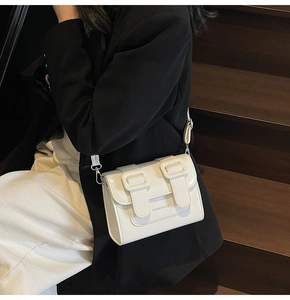 Detail shot of a minimalist cream white leather satchel with dual decorative buckles