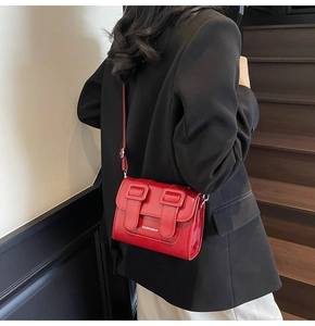 Detail of a bright red satchel bag with flap design and decorative buckle straps