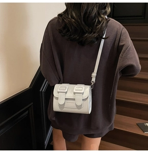 Detail of light grey satchel bag on shoulder with adjustable strap and brand logo
