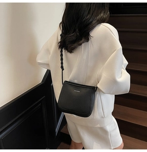 Detail of black pebbled leather bucket bag with woven strap and branding in a lifestyle shot