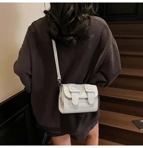 Detailed view of cream leather crossbody bag with adjustable straps on a wooden staircase