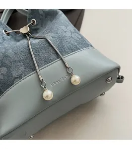 Detail of blue bucket bag showing textured fabric, metal drawstring and pearl charm