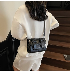 Detail of a black crossbody satchel with glossy finish and buckle straps on wood stairs