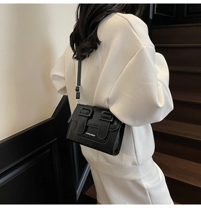 Close-up of black matte PU leather crossbody bag featuring dual buckle straps and silver hardware