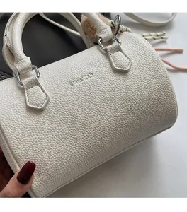Detailed macro view of white litchi pattern leather and embossed logo on the barrel bag
