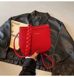 Detail of red pebbled leather bucket bag with braided handle and metallic logo