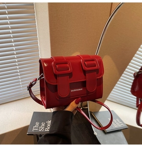 Detail of red patent leather crossbody bag with buckle straps and minimalist white logo