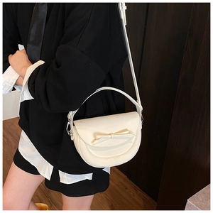 Gros plan du sac de selle blanc avec nœud et bandoulière réglable porté par le mannequin