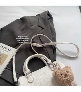 Detailed view of white lychee leather barrel bag with adjustable strap and bear charm