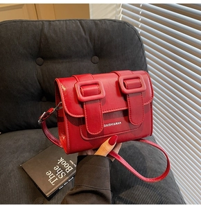 Detail of red leather satchel bag with dual buckle closure and slim shoulder strap