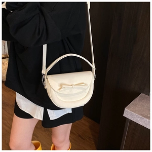 Détail d'un sac bandoulière demi-lune blanc crème avec un nœud élégant et une bandoulière