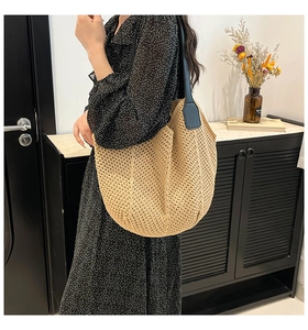 Close-up of beige woven straw tote bag with black leather straps on a model