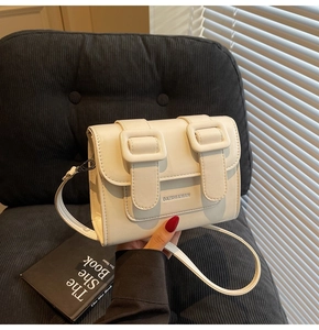 Detail of cream white faux leather satchel with double buckle straps and metal logo