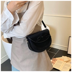 Détail du sac selle demi-lune noir avec nœud porté par un mannequin dans un cadre chic