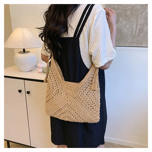 Dettaglio borsa tote in paglia intrecciata con nappe decorative e motivi a maglia traforata