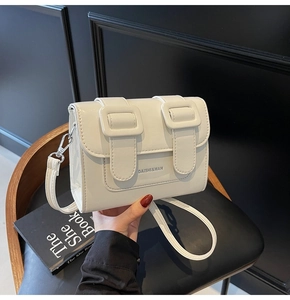 Detail shot of white PU leather crossbody bag with decorative buckles on a black chair