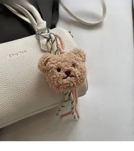 Detail of a brown plush bear bag charm with colorful woven ropes on a white leather handbag