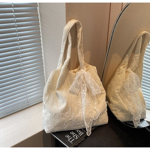 Detailed view of floral embroidery and large lace bow on a cream fabric tote bag