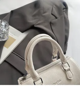 Detail of cream lychee leather cylinder bag with silver hardware and embossed logo