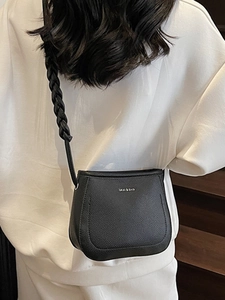 Chic black bucket bag with lychee texture and woven strap shown on model's shoulder