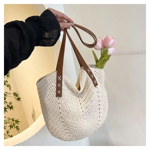 Detail der handgewebten Strohtasche mit Ledergriffen und dekorativen weißen Kreuznähten