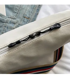Detail view of smooth dual zippers and colorful striped canvas strap on casual cream bag