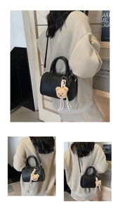 Close-up of black cylinder leather bag with plush bear charm and striped ribbon detail