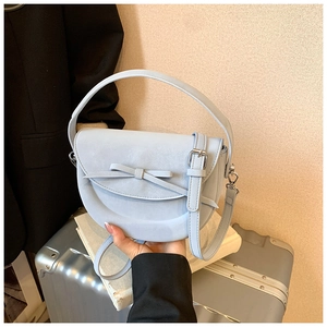 Gros plan d'un sac selle bleu clair avec nœud décoratif et bandoulière amovible