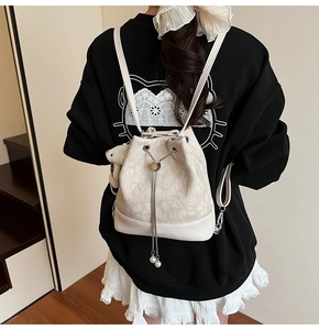Detail of cream drawstring bucket backpack with floral texture and pearl pendant