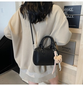 Detail view of a black lychee texture Boston bag with cute plush bear charm on a model