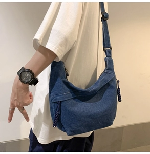 Detail of blue denim crossbody bag with contrast stitching and decorative knotted zippers