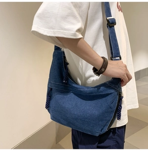 Detail of dark blue denim crescent bag showing adjustable strap and zipper closure