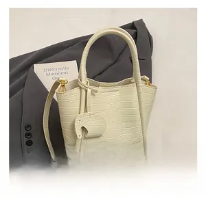 Detail of white crocodile pattern bucket bag with cylindrical handles and elephant charm